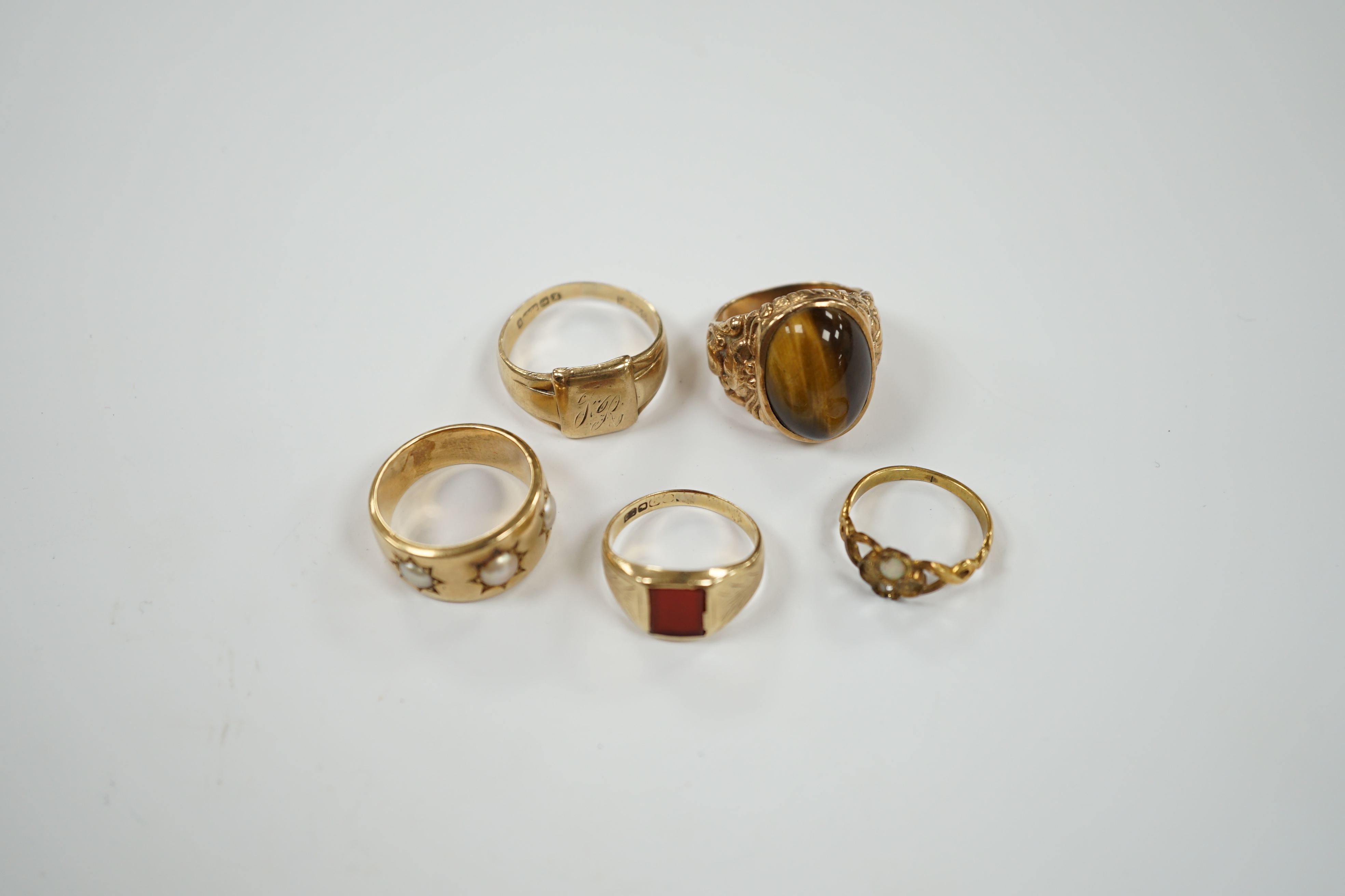 A 9ct gold signet ring, a gold and carnelian set signet ring and three yellow metal rings one set with three split pearls and one set with tiger's eye quartz cabochon, gross weight 29.7 grams.